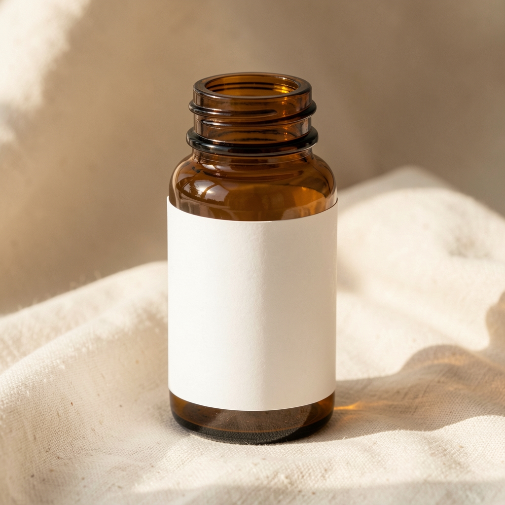 Kalem Complete Daily Stamina Complex — amber glass supplement bottle with clean typographic label on a warm cream linen surface, morning natural light filtering from the left